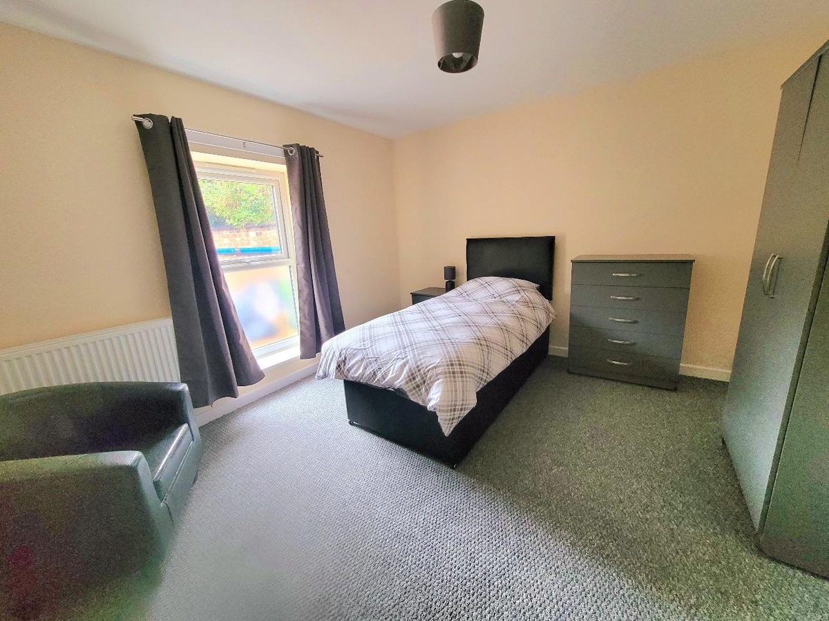A furnished single bedroom in Commlyncx supported accommodation with bed, wardrobe, drawers and armchair